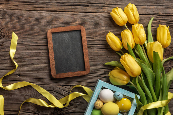 Yellow tulips in a paper bag, a nest with Easter eggs on a wooden background. Top view with copy space. - Foto, Imagem
