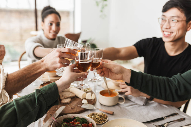 Κοντινό πλάνο διεθνών παρέα κρατώντας ποτήρια κρασί στα χέρια. Νέους συναδέλφους γιορτάζει χαρωπά μαζί δαπάνες χρόνο για γεύμα σε καφετέρια - Φωτογραφία, εικόνα