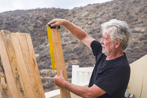 Felnőtt nyugdíjas férfi munka szabadtéri, mint ács vesz intézkedés méretei fa asztal - Fotó, kép