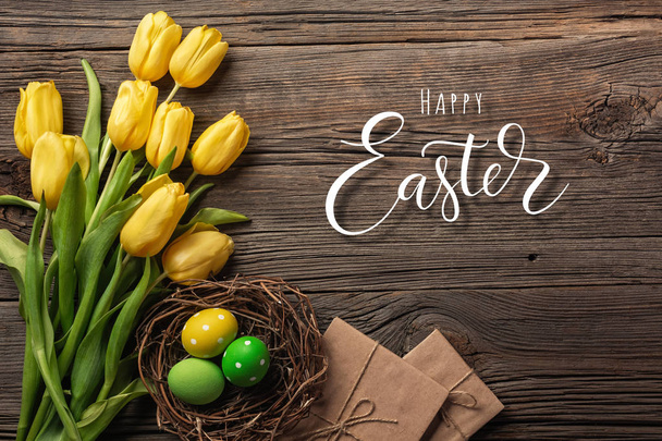Yellow tulips in a paper bag, a nest with Easter eggs on a wooden background. Top view with copy space. - Photo, Image