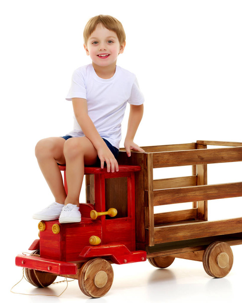 Μικρό αγόρι παίζει με ένα ξύλινο αυτοκίνητο. - Φωτογραφία, εικόνα