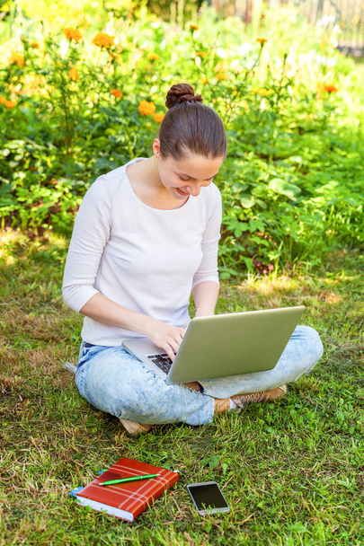 Freelance business concept. Young woman sitting on green grass lawn in city park working on laptop pc computer. Lifestyle authentic candid student girl studying outdoors. Mobile Office - Fotografie, Obrázek