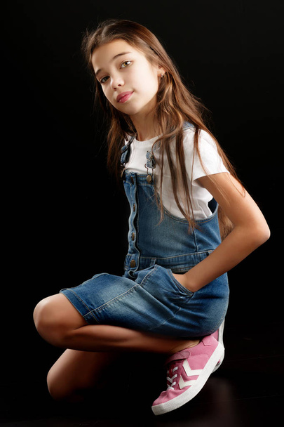 Little girl in denim clothes on a black background. - Fotó, kép