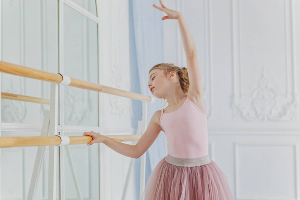 Mladá klasická baletka ve třídě tance. Krásná elegantní balerína praxe baletní pozice v růžové sukně sukně tutu v blízkosti velkého zrcadla v bílé světelné hale - Fotografie, Obrázek