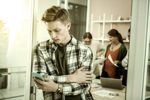 Handsome student wearing squared shirt holding blue smartphone - Fotografie, Obrázek