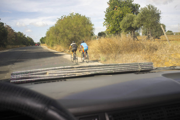 Conduciendo lentamente detrás de dos ciclistas en la carretera del campo. Vista desde el interior del coche
 - Foto, Imagen
