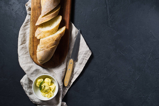 Sliced French baguette, butter and a sprig of rosemary on a wooden chopping Board. Black background, top view, space for text - Φωτογραφία, εικόνα