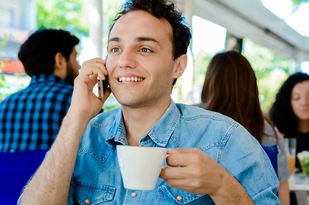Młody mężczyzna siedząc w kawiarni i przy użyciu smartfonu. - Zdjęcie, obraz