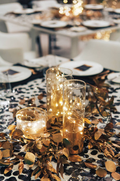 Mesa de jantar decorada em preto e ouro. Garland em um frasco de vidro. Decorações de casamento
 - Foto, Imagem