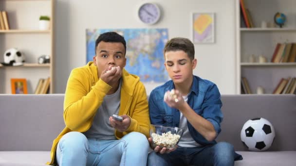 Anxious teenage friends watching football match on TV and eating popcorn leisure - Imágenes, Vídeo