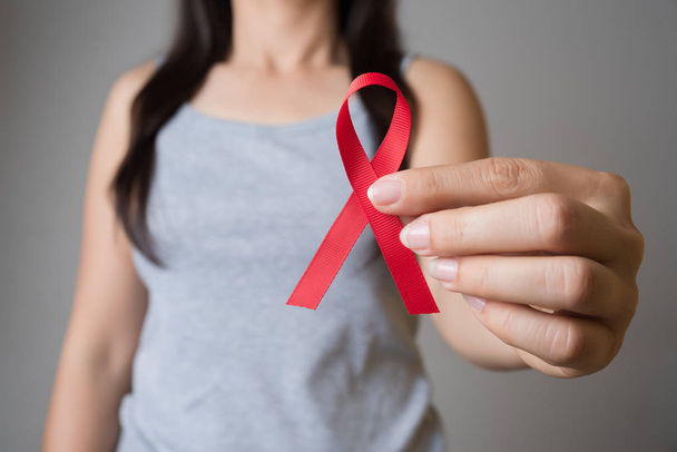 Closeup woman hand holding red ribbon HIV, world AIDS day awareness ribbon. Healthcare and medicine concept. - Foto, Bild