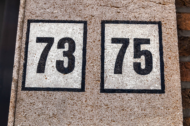 Casa número setenta e três, setenta e cinco 73 75 em preto sobre fundo branco na parede branca renderizada na Bélgica
 - Foto, Imagem