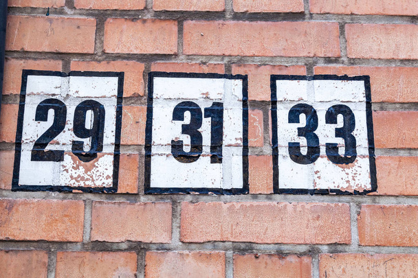 Hausnummer neunundzwanzig, einunddreißig, dreiunddreißig 29, 31, 33 schwarz auf weißem Hintergrund auf roten Hausziegeln in Belgien - Foto, Bild