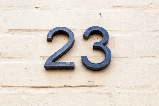 Casa número vinte e três 23 de metal em tijolo branco pintado na Bélgica
 - Foto, Imagem