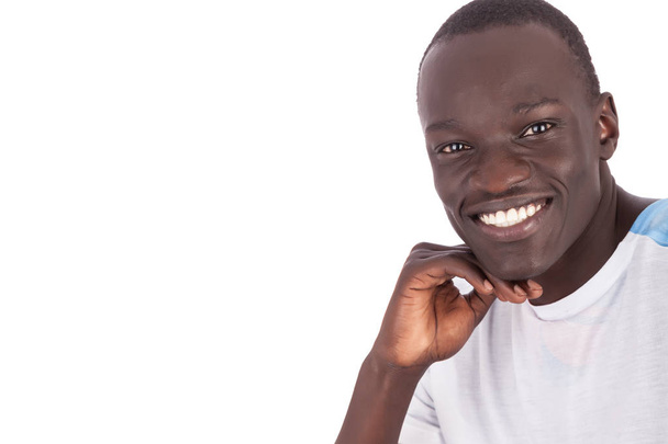 Κοντινό πλάνο του προσώπου όμορφος νεαρός άνδρας σουδανικής κάμερα σε άσπρο tshirt, χαμογελώντας με τα άσπρα δόντια που δείχνει χαρά χαρά και εμπιστοσύνη σε οριζόντια μορφή με χώρο αντίγραφο που απομονώνονται σε λευκό φόντο. - Φωτογραφία, εικόνα