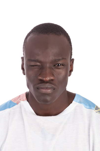 Joven hombre sudanés guapo guiñando un ojo derecho sin sonrisa cara recta, boca cerrada cara a cámara en camiseta blanca, en retrato con espacio de copia aislado sobre fondo blanco
 - Foto, imagen