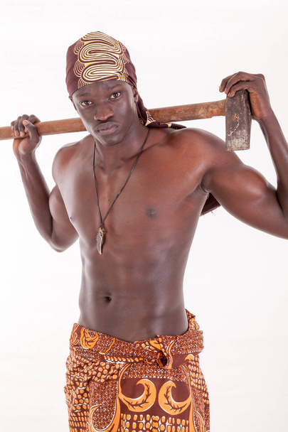 Homem sudanês com roupas culturalmente apropriadas com machado ou divisor de bloco sobre o ombro, tronco nu, saia batik e faixa de cabeça
 - Foto, Imagem