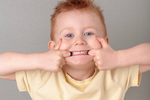 Πύρινη κοκκινομάλλα νεαρό αγόρι δάχτυλα στο στόμα της που δείχνει τα δόντια του τραβώντας ένα πρόσωπο, φοράει κίτρινο πουκάμισο σε οριζόντια μορφή με αντίγραφο χώρο. Meme/αφίσα της χαριτωμένο κοκκινομάλλα αναιδή υγείας, κοιτάξτε την έννοια τα δόντια μου - Φωτογραφία, εικόνα