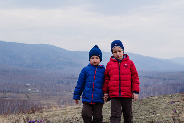 tired children walk outdoors in the mountains in the spring. Two boys in warm jackets and hats - Photo, image
