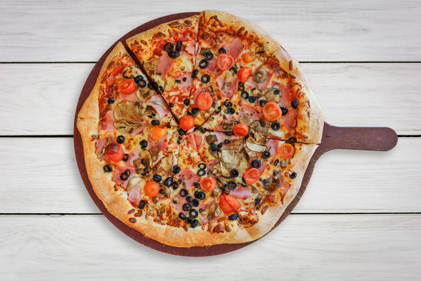 Вид сверху традиционной пиццы с ветчиной, грибами, помидорами вишни, моцареллой, черными оливками на деревянном белом столе (высокие детали)
). - Фото, изображение