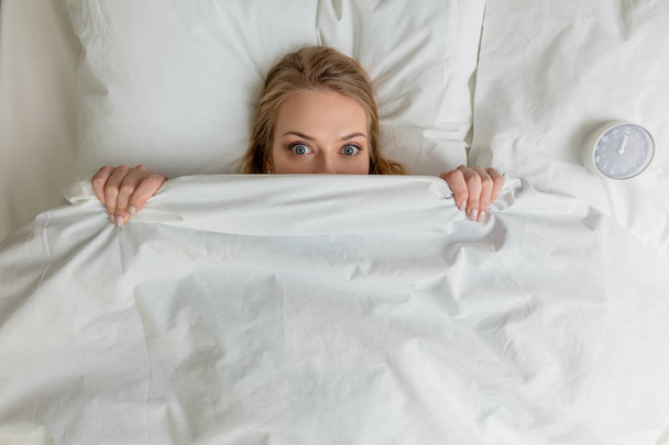 pleasant blonde girl hiding under the blanket and looking at the camera - Fotoğraf, Görsel