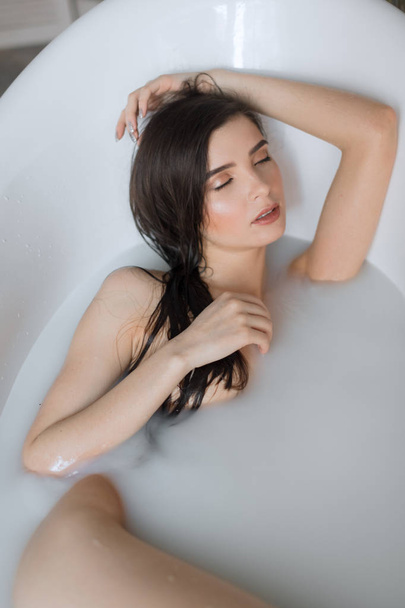 Attractive girl with open eyes takes a milk bath, touching her hair - Fotó, kép