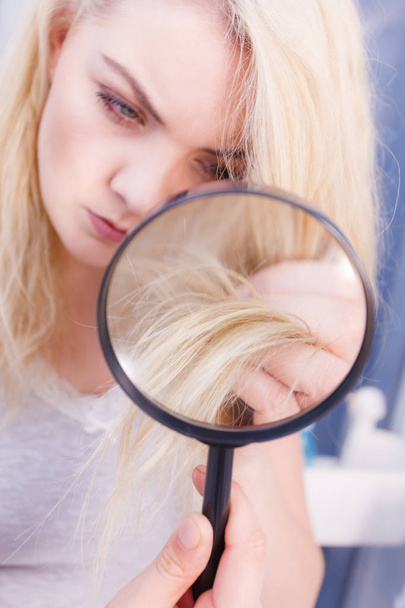 Saç bakımı, beyazlatma konseptinin kötü etkileri. Mutsuz kadın büyüteçle sarı saçlarına bakıyor. - Fotoğraf, Görsel