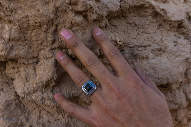 Käsi nuorelta mieheltä, jolla on hopeasormus kaiverrettuna mustalla kivellä muinaiseen Mervin muuriin, Turkmenistanin ja Seljukin valtakunnan pääkaupunkiin. Merv. Kansallinen perintö. Kunnianosoitus esi-isille
 - Valokuva, kuva
