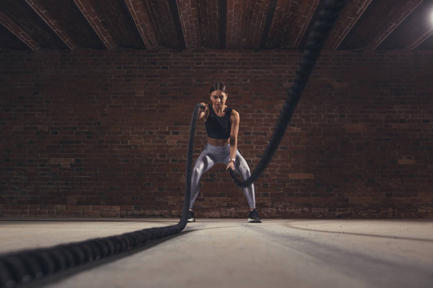 Joven mujer caucásica haciendo ejercicio con cuerdas de batalla en un gimnasio
 - Foto, imagen