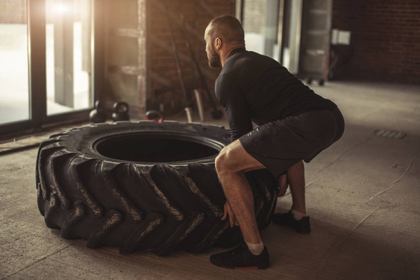 Young caucasian muscular man flipping heavy tire in gym - Fotoğraf, Görsel