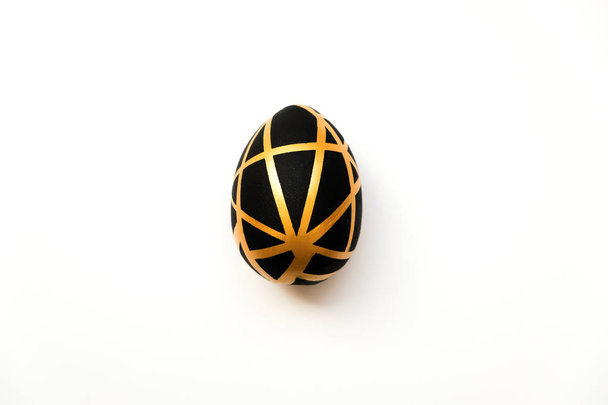 Великоднє золоте яйце з геометричним чорним візерунком ізольовано на білому тлі. Концепція мінімального Великодня. Вид зверху, плоский
 - Фото, зображення