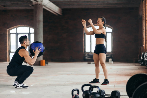 sporty man and woman throwing a fitness ball to each other in the sport center - 写真・画像