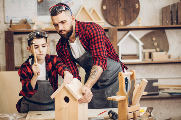 Father and his son working together in a wooden workshop, building a birdhouse - Foto, imagen