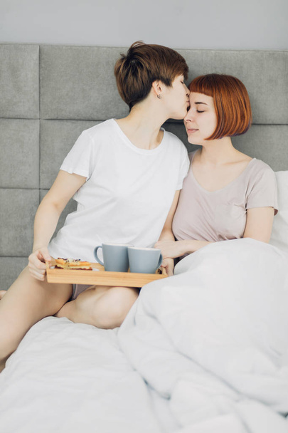 attractive girl holding breakfast and kissing her girlfriend - Foto, afbeelding