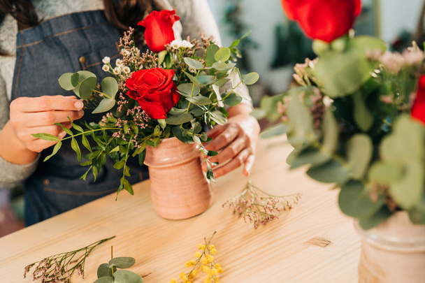 Woman florist makes a red roses bouquet on wooden table - 写真・画像