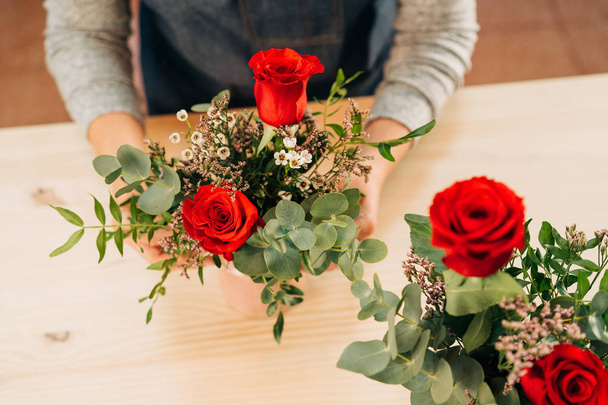 Woman florist makes a red roses bouquet on wooden table - Photo, Image