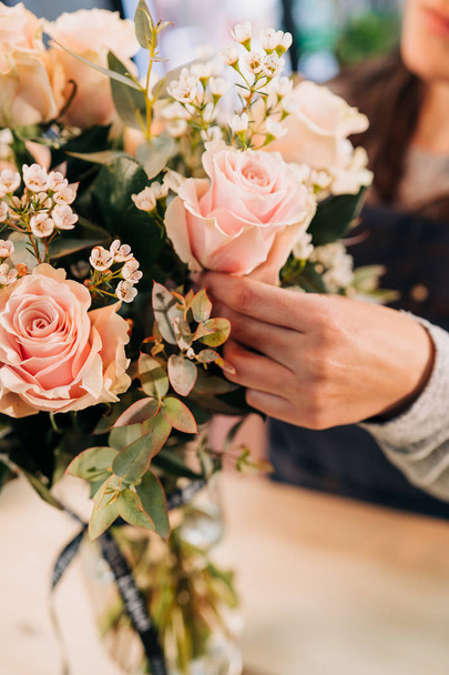 Woman florist makes a pink roses bouquet on wooden table - Valokuva, kuva