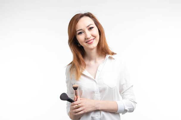 Make-up-Artist, Schönheit und Menschen Konzept - schöne koreanische junge Frau hält Make-up-Pinsel auf weißem Hintergrund - Foto, Bild