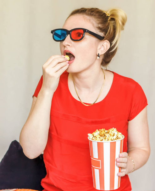 Retrato de una joven riendo usando gafas 3d comiendo palomitas de maíz sentado en un sofá
 - Foto, imagen