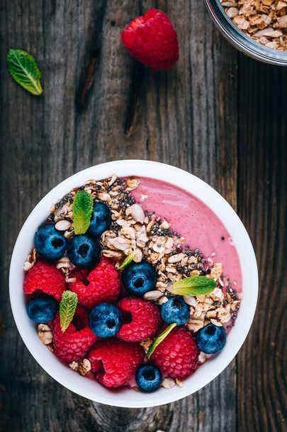 Acai smoothie and granola bowl with fresh raspberries and blueberries on wooden background - Foto, imagen