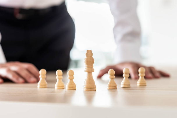 Chess pieces of king and pawns placed on office desk with king as the leader and businessman in background in a conceptual image. - Photo, Image