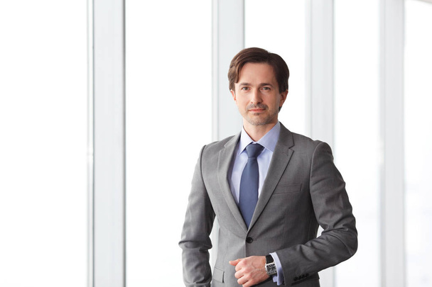 Portrait of handsome businessman standing near windows in office - Fotó, kép