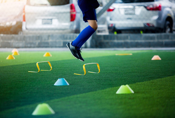 少年サッカー ジョギングやマーカーと黄色のハードル間をジャンプします。サッカーのトレーニング. - 写真・画像