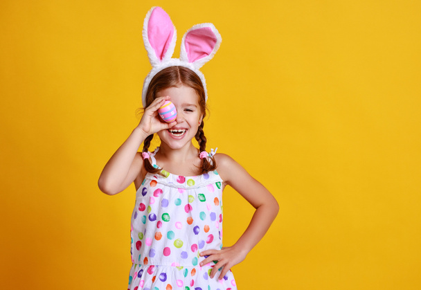 lustiges fröhliches Kindermädchen mit Ostereiern und Hasenohren auf gelbem Hintergrund - Foto, Bild