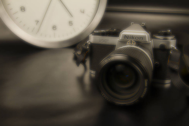 The frenzy of today's times in contrast with the past. A modern design wall clock next to a vintage camera on a black background with sepia and orton effects - Photo, Image
