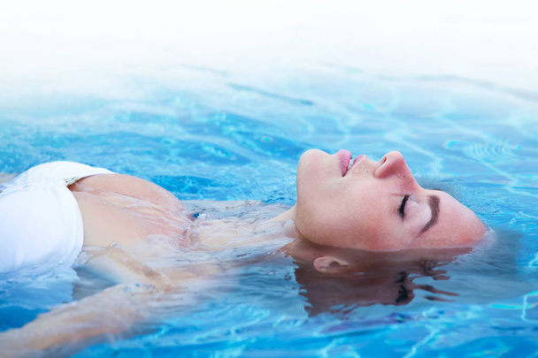 Girl in bikini relaxing floating in blue water of swimming pool - Photo, image