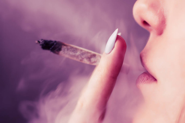 Een vrouw rookt cannabis onkruid, een gezamenlijke en een aansteker in zijn handen. Roken op een zwarte achtergrond. Begrippen medisch marihuanagebruik en legalisatie van de cannabis. Op een zwarte achtergrond roze verven - Foto, afbeelding