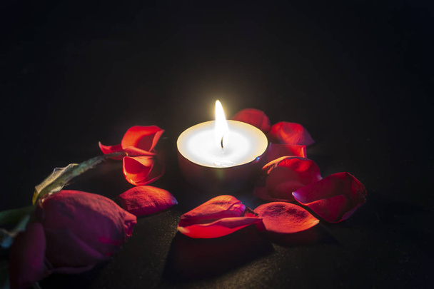Tea candle and red rose petals with shallow depth of focus with reflection on black background - Foto, immagini