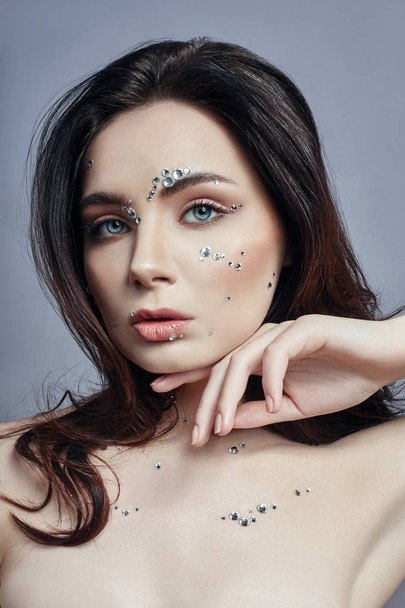 Art portrait of a woman with large crystals of rhinestones on her face, chest and body. Perfect makeup, skin care, professional cosmetics. Girl's face with diamonds on the skin close-up - Photo, image