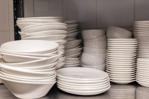 Montón de placas de porcelana blanca de cerámica limpia en un estante de metal en la parte posterior del restaurante. Concepto de preparación para un banquete, catering, buffet
 - Foto, imagen